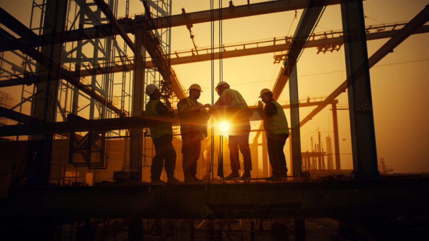 Construction crew in high-visibility PPE on a structural steel frame at sunset
